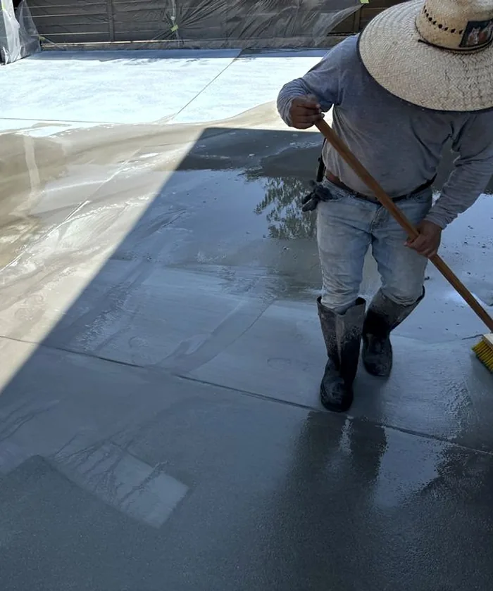 A finisher pulling a broom across a wet slab in the sun