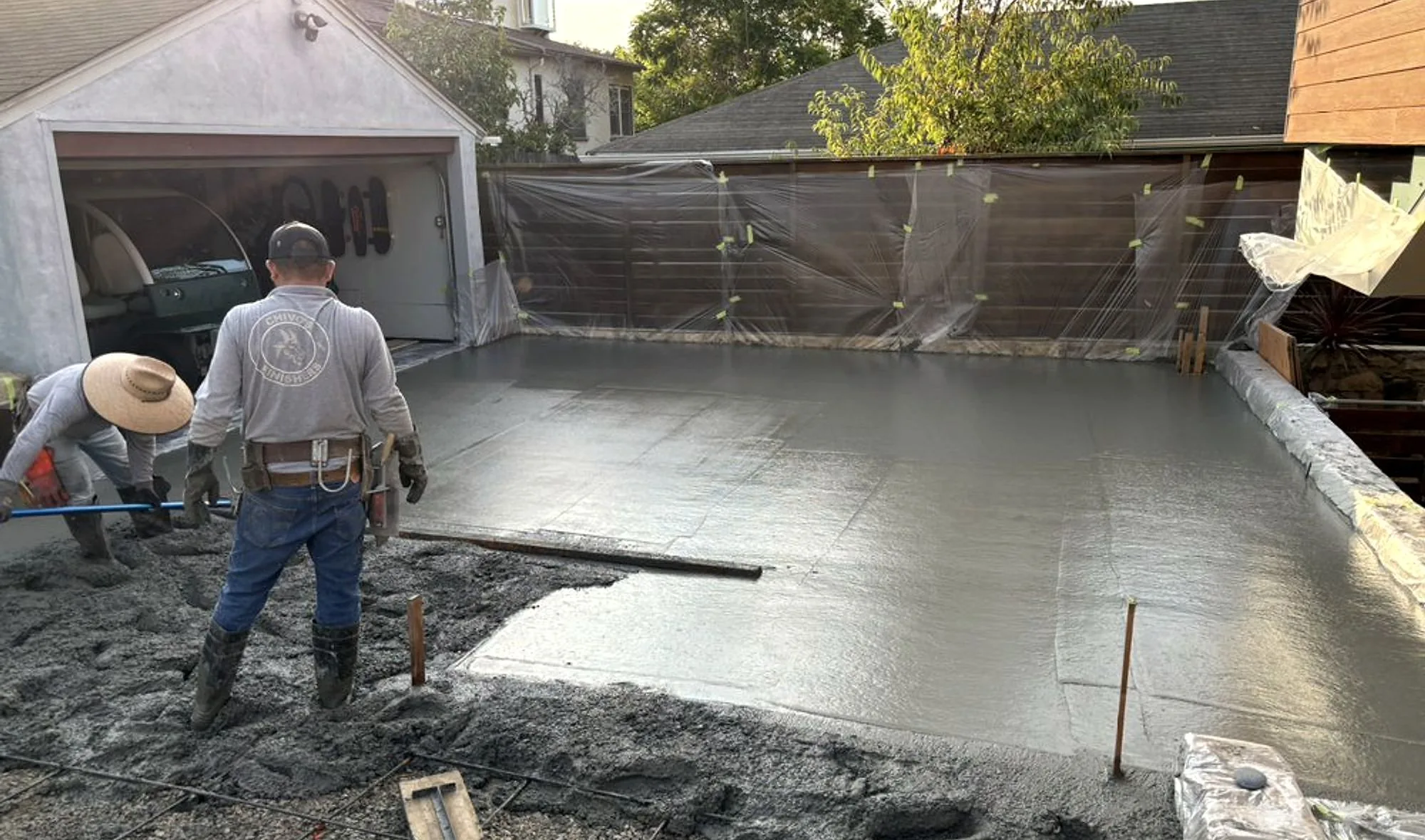 Two finishers screeding a fresh driveway pour at last light, raw concrete in the foreground running out to a smooth flat slab
