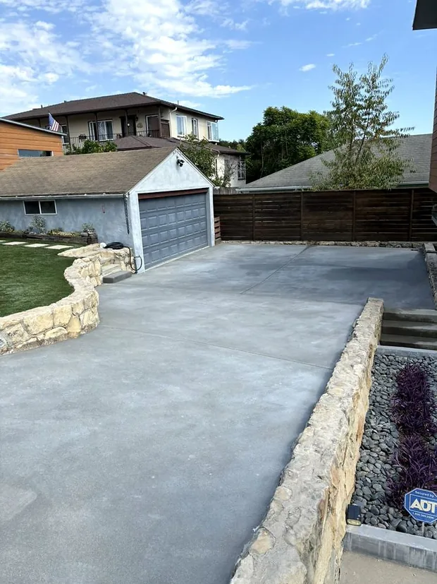 A finished concrete driveway running clean up to a garage between a stone wall and a fence