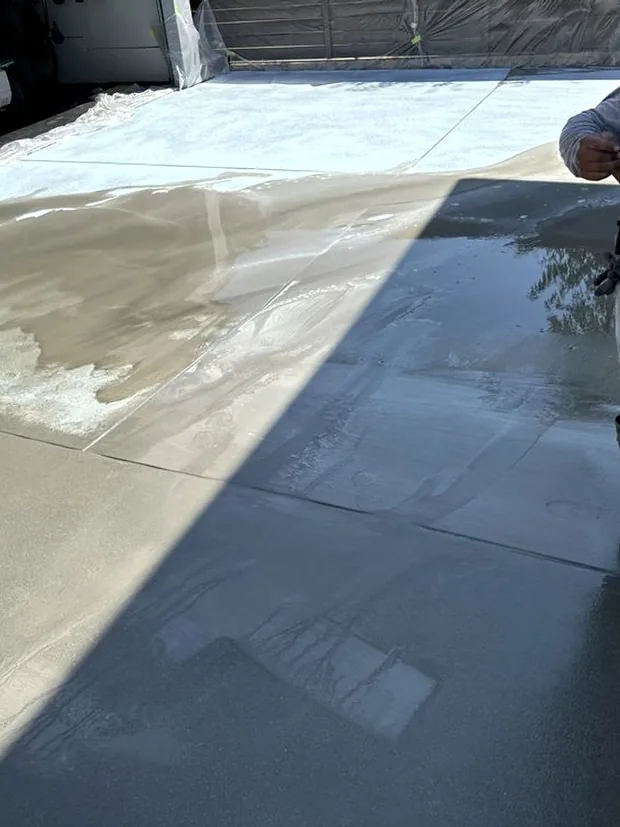 A finisher in a straw hat pulling a broom across a wet slab
