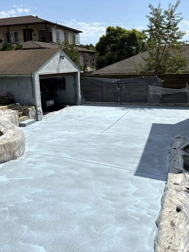 A freshly poured pale slab running up to a garage, edged against a stone wall