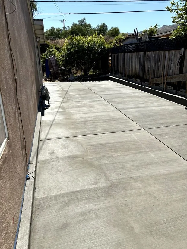 A narrow side yard poured as a clean concrete walkway between wall and fence